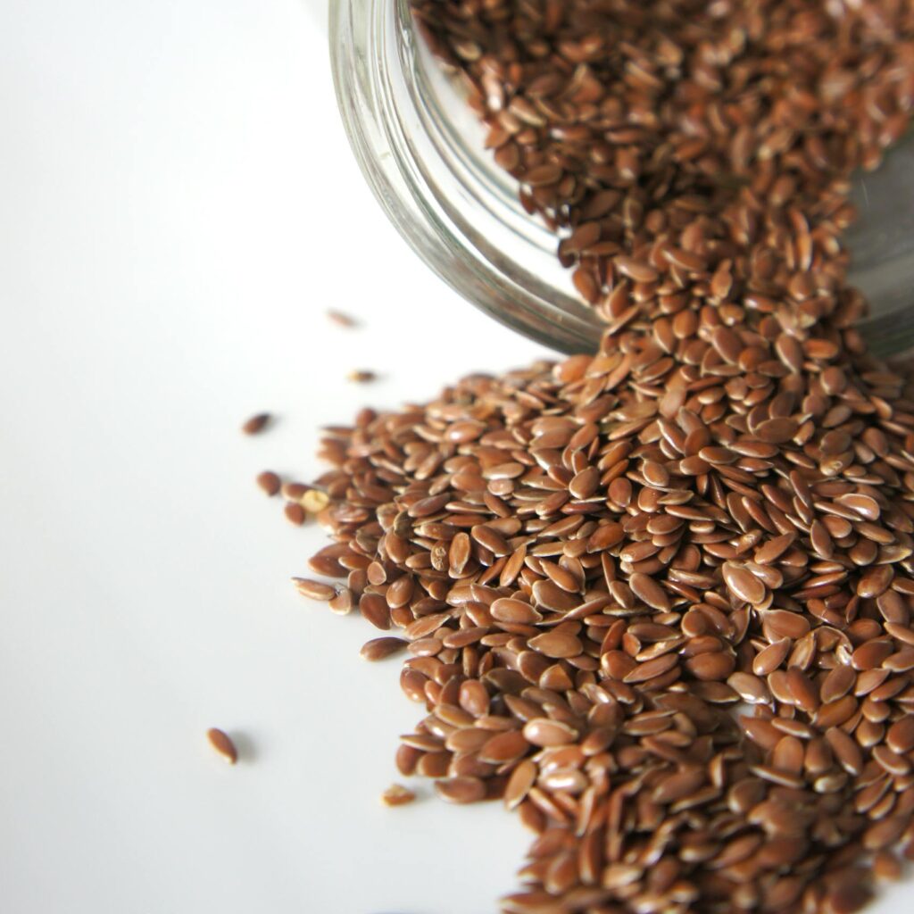 High angle view of flaxseeds spilling from a jar onto a white surface. Perfect for health and food concepts.