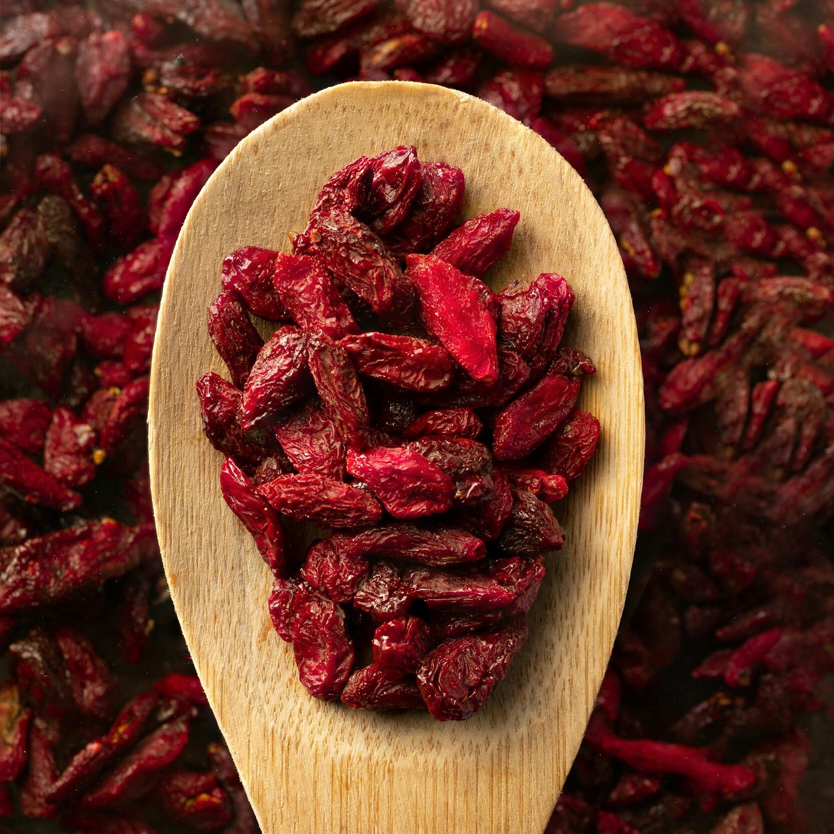 Top view of dried goji berries on a wooden spoon, emphasizing natural texture and rich color.