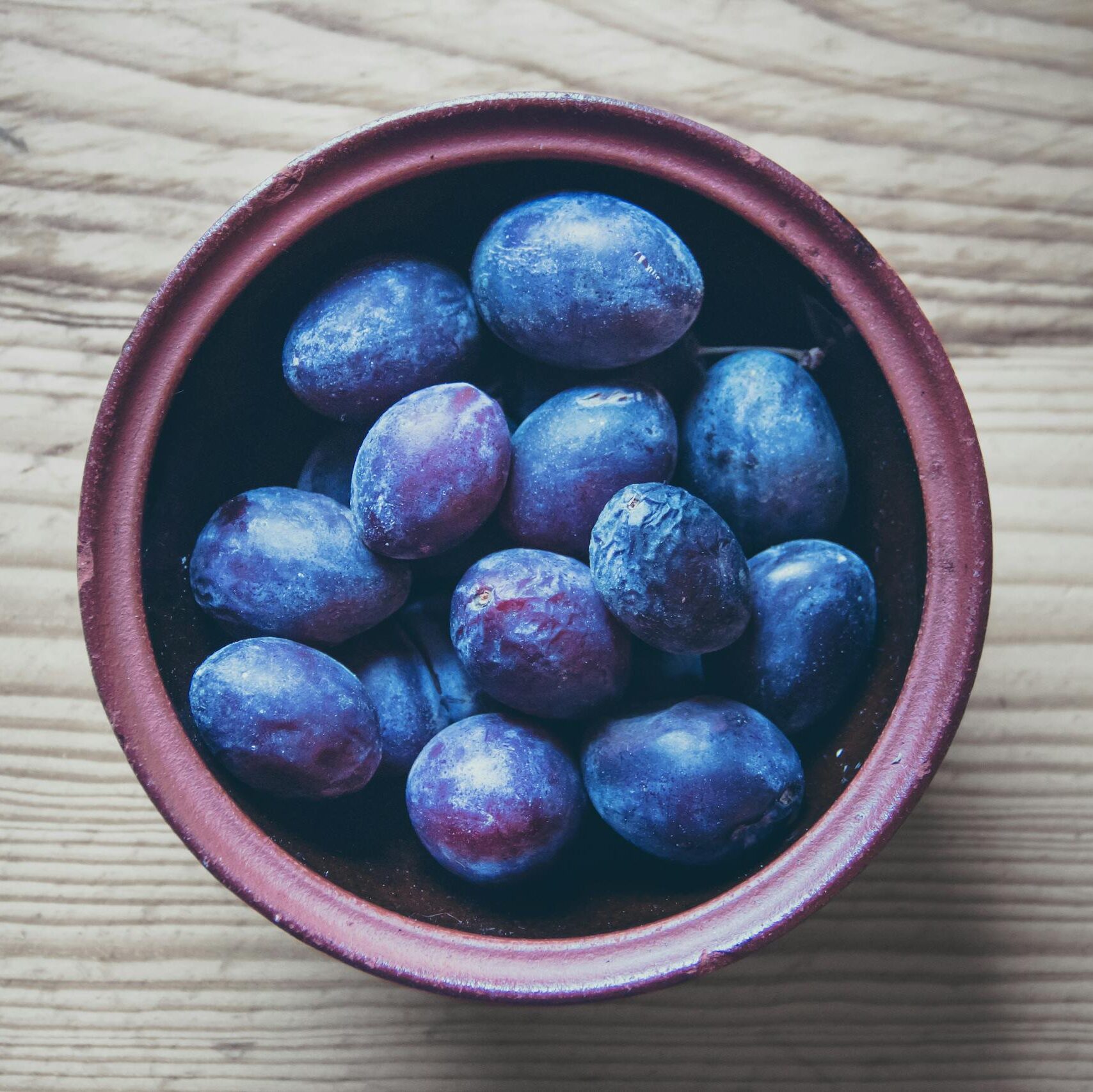 Top view of fresh organic plums in a rustic bowl on a wooden table, perfect for healthy diet themes.
